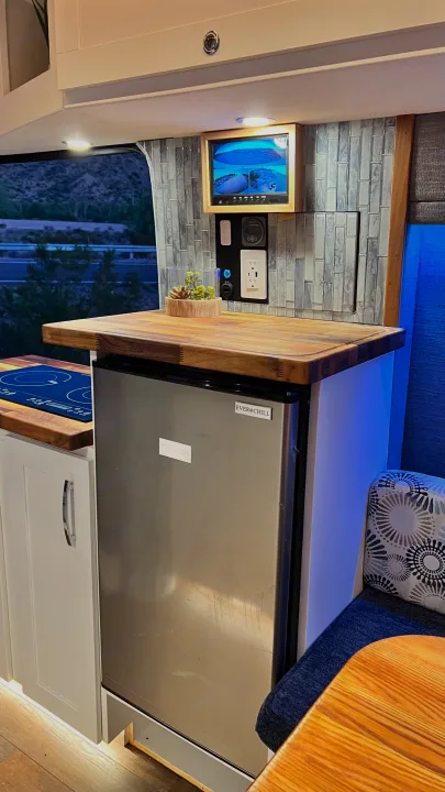 This modern RV rental kitchenette features a stainless steel fridge, induction cooktop, and tiled backsplash with monitor.. Ford Transit 2019