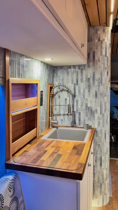 This rv rental features a custom kitchen with a butcher block countertop, sink, and stylish tiled backsplash, perfect for mobile living.. Ford Transit 2019