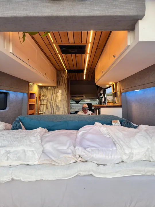 Experience van life comfort in this rv rental. A bed's view reveals the sleek kitchen, custom interior, and driver's cab.. Ford Transit 2019