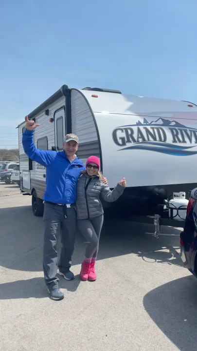 Joyful couple with their new Grand River travel trailer, perfect for an RV rental adventure. Sunny day.. Gulf Stream Grand River 22Mb 2024