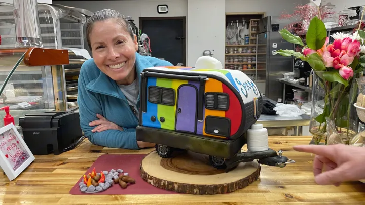 A baker proudly presents a vibrant rainbow RV cake, perfect for an RV rental adventure. Joy and edible fun!. Gulf Stream Grand River 22Mb 2024