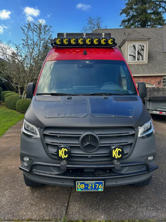Customized red and black Mercedes Sprinter van, an ideal RV rental, with rooftop and front KC lights, and hood solar panels.. Mercedes Sprinter 2022