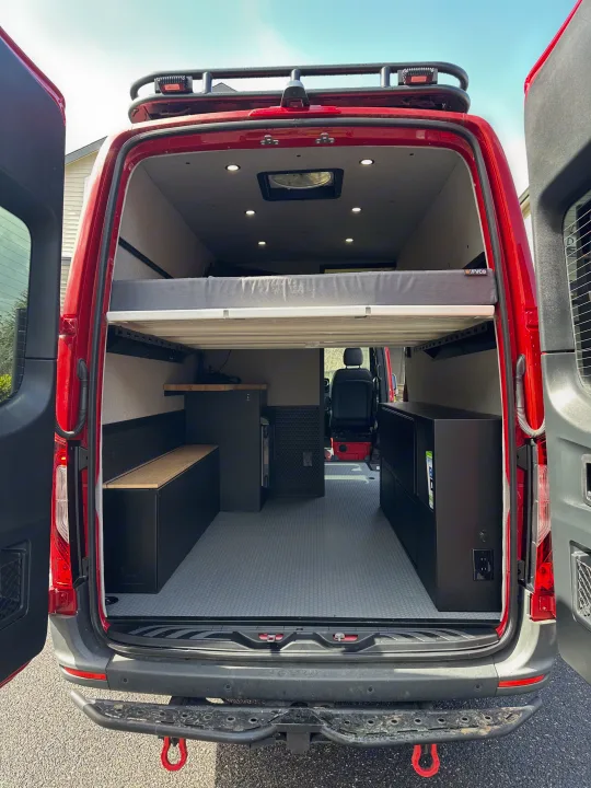 Spacious red camper van interior for your next RV rental adventure, featuring a raised bed and storage.. Mercedes Sprinter 2022