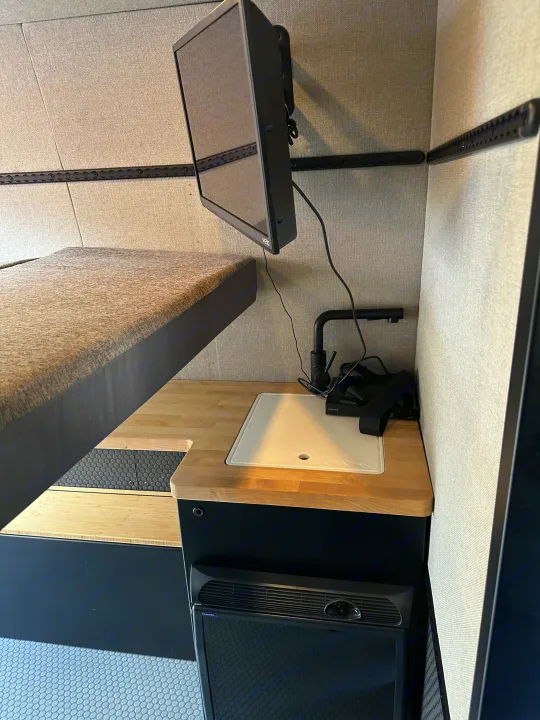 Modern RV rental interior with bunk bed, wall-mounted TV, wood counter, sink, & Engel fridge. Compact living.. Mercedes Sprinter 2022