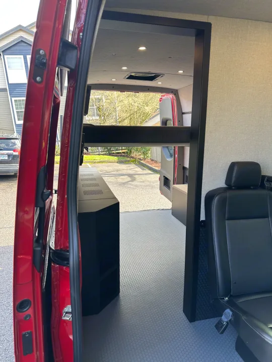 Interior view of a red van conversion with a bunk bed, counter, and swiveling seat, ideal for an RV rental.. Mercedes Sprinter 2022