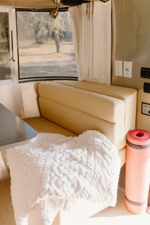 Cozy RV rental interior with comfy seating, a plush white blanket, and a yoga mat, offering a peaceful window view of nature.. Airstream Flying Cloud 2017