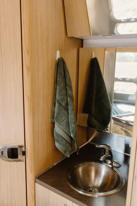 RV rental's small bathroom with a green hand towel, stainless steel sink, mirror, and wooden walls.. Airstream Flying Cloud 2017
