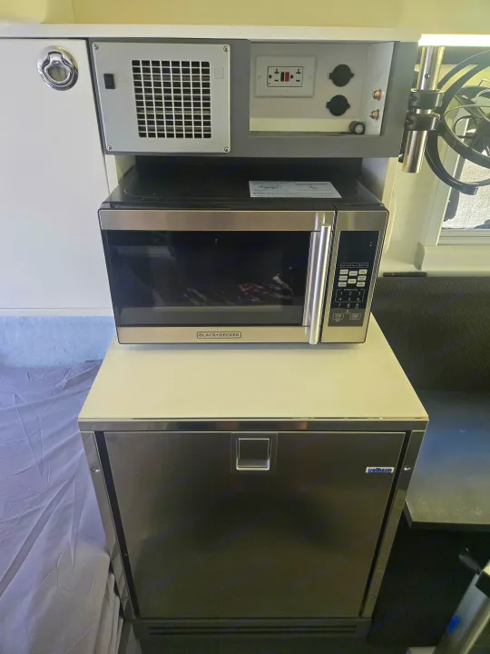 RV rental kitchen: Black+Decker microwave, Isotherm fridge, and electrical panel in a compact setup.. Bruder EXP-6 2018