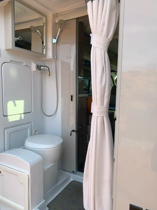 Inside an RV rental: a compact bathroom with toilet, shower, mirror, and tied-back privacy curtains.. Thor Motor Coach Scope 2023