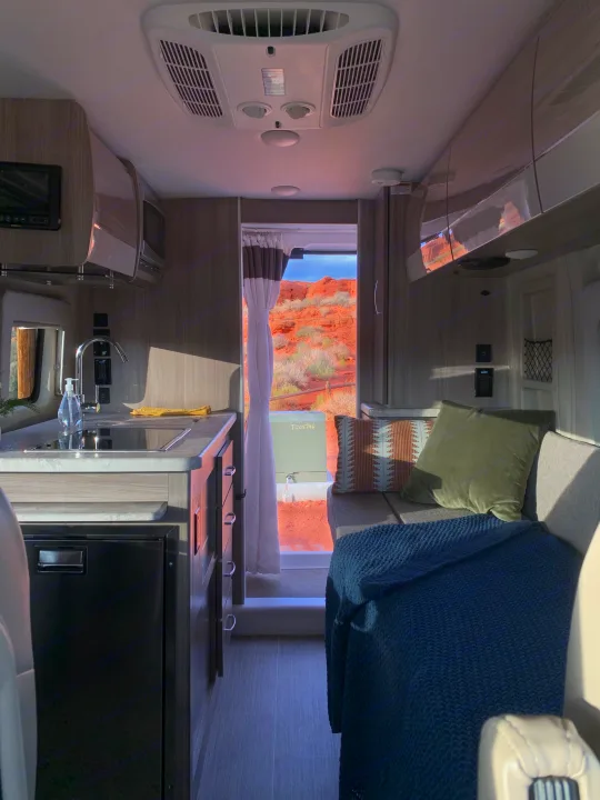 Modern rv rental interior with kitchen, cozy seating, and a breathtaking red rock desert view from the back door.. Thor Motor Coach Scope 2023