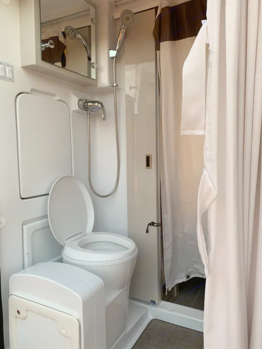 Clean, compact RV rental bathroom featuring a toilet, shower, and mirror.. Thor Motor Coach Scope 2023