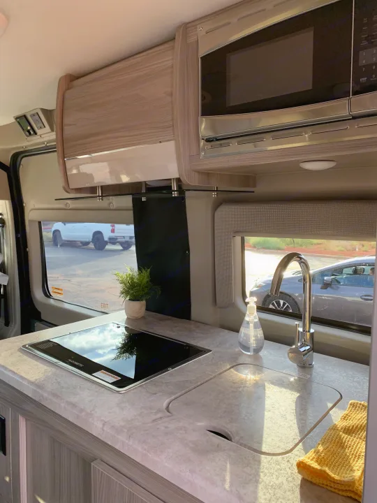 Experience cooking on the go! This RV rental features a compact kitchenette with sink, stovetop, microwave & sunny views.. Thor Motor Coach Scope 2023