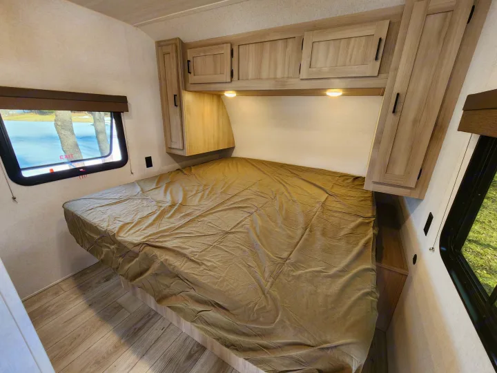 Cozy RV rental bedroom featuring a comfortable bed, overhead storage, and a winter wonderland window view.. East to West Silver Lake LE 2024