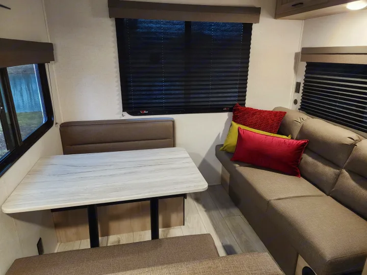 Inside an RV rental: a modern dinette with light-colored table and bench seating, plus a comfortable sofa with colorful pillows.. East to West Silver Lake LE 2024