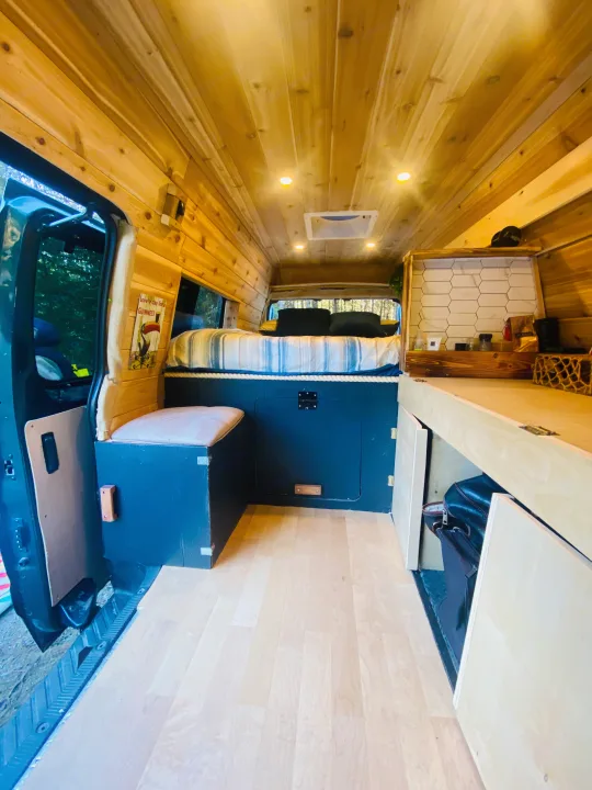 Cozy RV rental camper van interior: bed, wood paneling, and smart storage for your adventures.. Ford Econolline 250s 2001