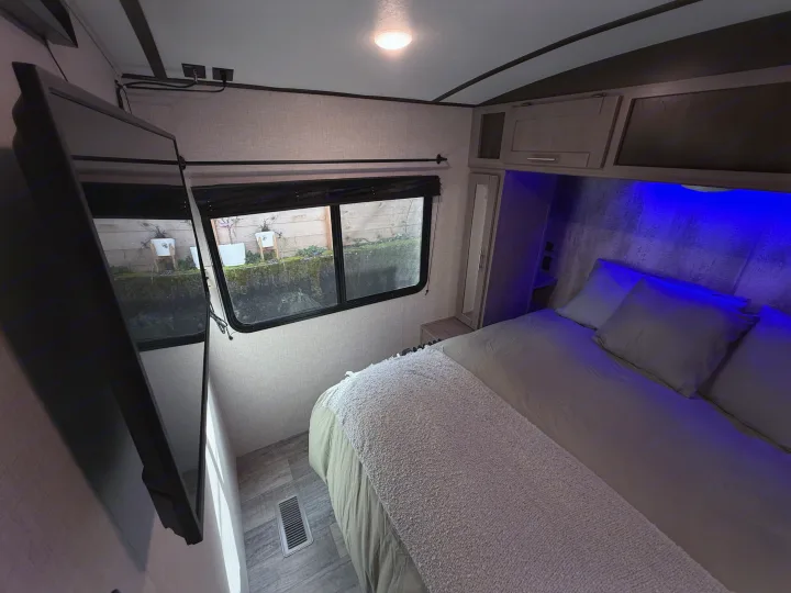 Cozy RV rental bedroom featuring a large bed, wall-mounted TV, and blue ambient lighting. View out window.. Crossroads Sunset Trail Super Lite 2021
