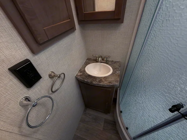 Inside an RV rental: a compact bathroom with a sink, wood vanity, and textured glass shower door.. Crossroads Sunset Trail Super Lite 2021