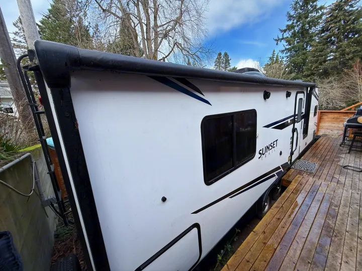 A modern white Sunset Trail travel trailer, ideal for an RV rental, parked on a wooden deck. Perfect for outdoor adventures.. Crossroads Sunset Trail Super Lite 2021