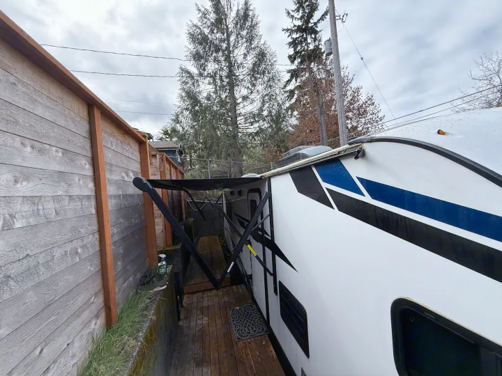 An RV rental is parked with its awning extended over a wooden deck, alongside a fence on a cloudy day.. Crossroads Sunset Trail Super Lite 2021