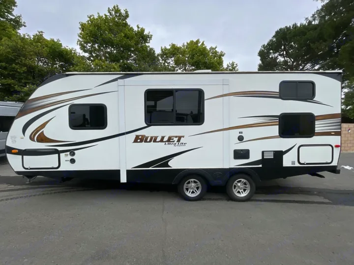 White Bullet Ultra Lite travel trailer RV rental. This modern camper, seen from the side, has sleek graphics & tinted windows.. Keystone RV Bullet Ultra Lite 2014