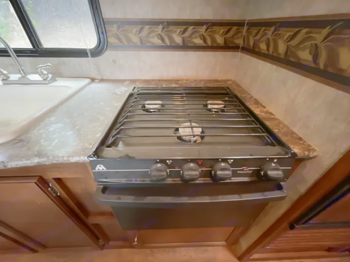 RV rental kitchen interior: sink, chrome faucet, granite-look counter, and a black 3-burner gas stove with oven controls.. Keystone RV Bullet Ultra Lite 2014