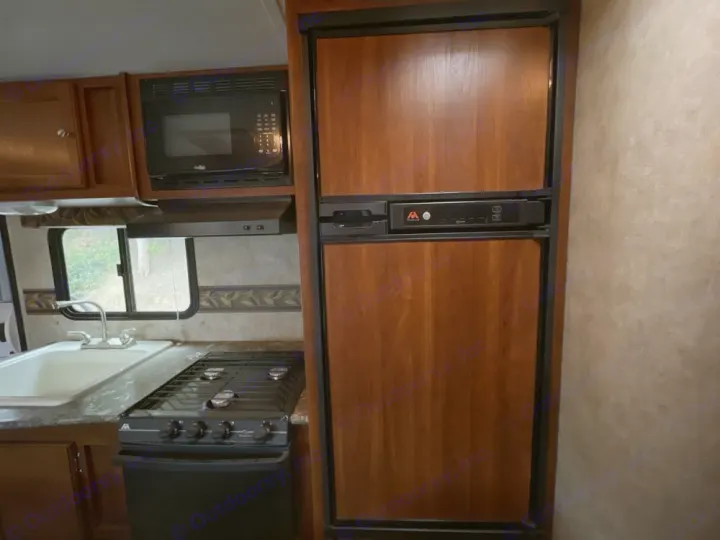 RV rental kitchen: Wood cabinetry, microwave, large fridge, stove, and sink.. Keystone RV Bullet Ultra Lite 2014