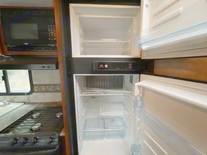Inside an RV rental kitchen, showing the open refrigerator, microwave above, and stovetop below the window. Essential RV appliances.. Keystone RV Bullet Ultra Lite 2014