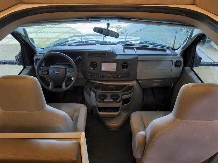 RV rental interior: Front cab with dashboard, steering wheel, and two captain's seats, visible through a rainy windshield.. East To West Entrada 2000NS 2025