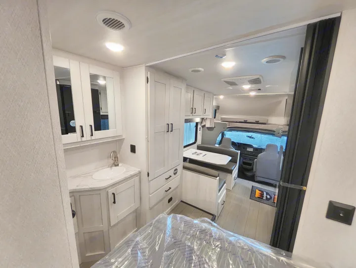 Inside a modern RV rental: light-toned bathroom vanity, tall storage, and dinette area leading to the driver's cabin.. East To West Entrada 2000NS 2025