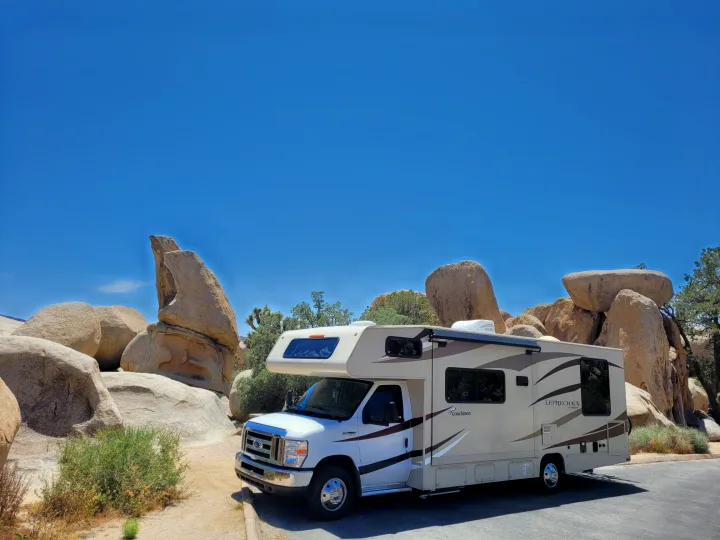 An RV rental, a Coachmen Leprechaun, parked amongst large desert boulders and sparse vegetation under a clear blue sky.. Forest River Coachmen Leprechaun 2018
