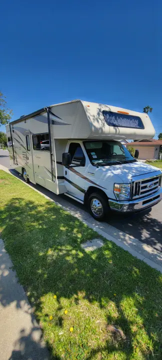 Spacious Class C RV rental, a white and beige motorhome, parked on a sunny residential street.. Forest River Coachmen Leprechaun 2018