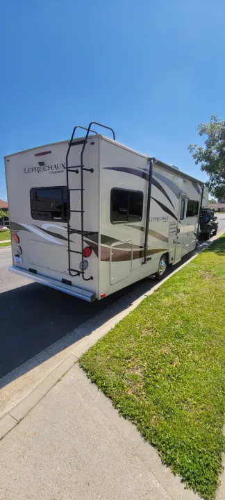 Spacious beige and brown Leprechaun RV, complete with a rear ladder, parked on a street. Ideal for your next rv rental adventure!. Forest River Coachmen Leprechaun 2018