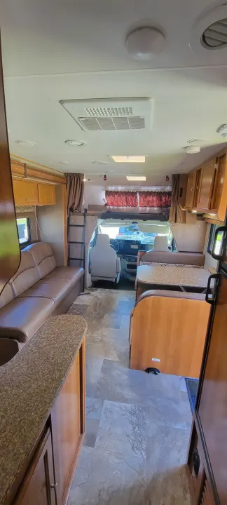 Inside a clean, spacious RV rental, showing the comfy lounge, dinette, and cockpit area with an overhead bunk.. Forest River Coachmen Leprechaun 2018