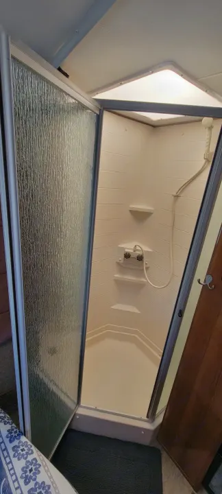 This RV rental shower features a compact design with a textured glass door, built-in shelves, and a handheld showerhead. Perfect for travel!. Forest River Coachmen Leprechaun 2018