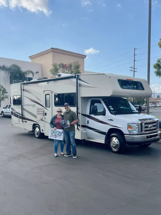 Smiling couple with their "Leprechaun" Class C RV rental, holding maps for their new adventure.. Forest River Coachmen Leprechaun 2018