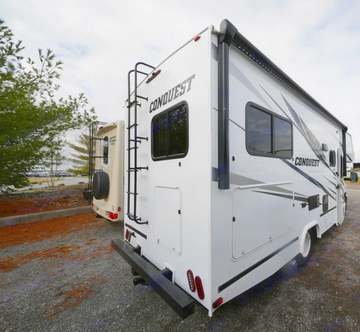 Rear view of a white Conquest RV rental, featuring a back ladder & side awning, parked on gravel. Perfect for travel.. Gulf Stream Conquest 2023