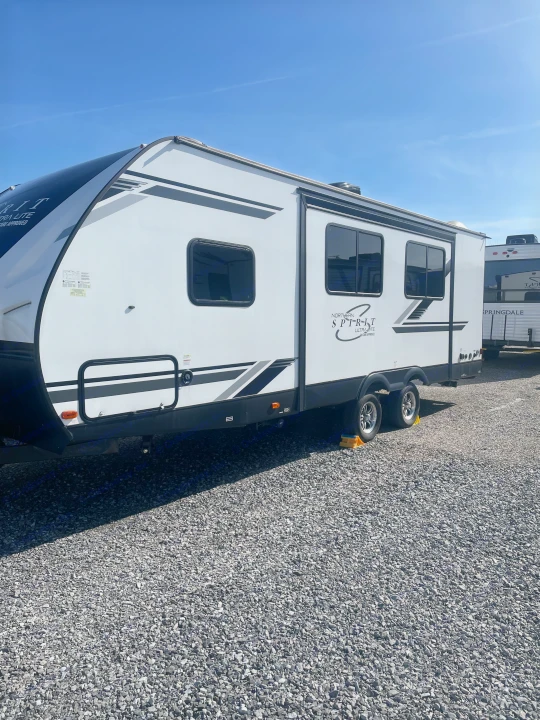 This white Northern Spirit Ultra Lite travel trailer is parked on a gravel lot, ready for your next rv rental.. Coachmen 2557RB 2021