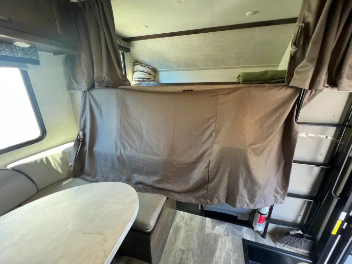 Cozy RV rental interior featuring a bunk bed with privacy curtain and a dinette area with seating and a table.. Gulf Stream Conquest 2023