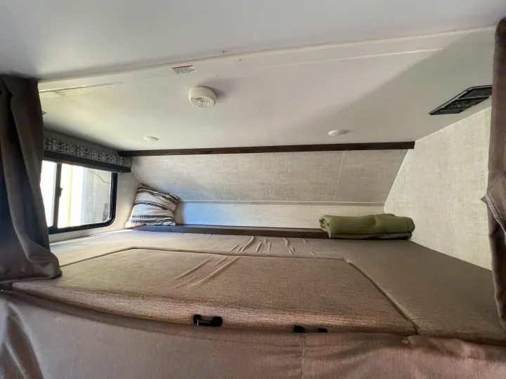Cozy RV rental cab-over bunk interior with mattress, window, pillow, and folded blanket for a restful sleep.. Gulf Stream Conquest 2023