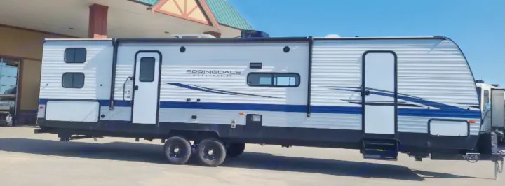 A modern white and blue Springdale Keystone XL travel trailer, with two entry doors and an awning, ideal for an rv rental.. Keystone RV Springdale 2020