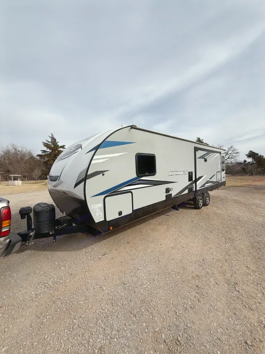 A modern grey Alpha Wolf Cherokee travel trailer, perfect for an rv rental, is parked on a gravel lot under cloudy skies.. Forest River Cherokee Alpha Wolf 2022