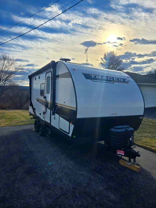 A new white Tracer travel trailer is parked on a driveway on a sunny day. Looks like a great candidate for an RV rental.. Prime Time Tracer LE 2024