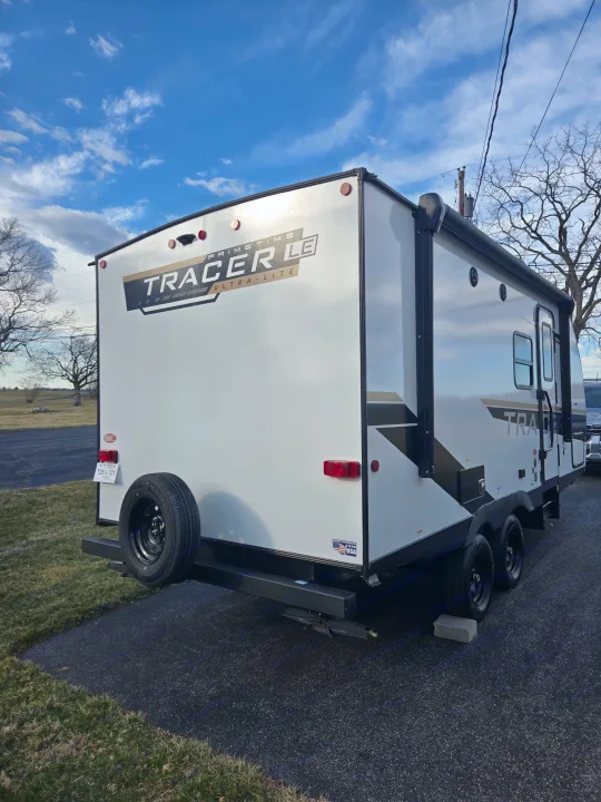Rear view of a white Primetime Tracer LE travel trailer, ready for RV rental. Parked on an asphalt lot with a spare tire.. Prime Time Tracer LE 2024