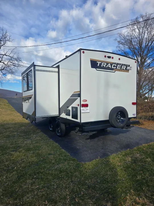 White Tracer LE travel trailer, an rv rental, parked on an asphalt lot with its slide-out extended for outdoor living.. Prime Time Tracer LE 2024