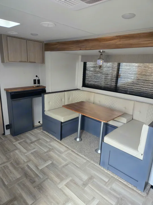 An RV rental's modern interior, showing a blue-based dinette with cream cushions, wooden table, and herringbone floor.. Prime Time Tracer LE 2024
