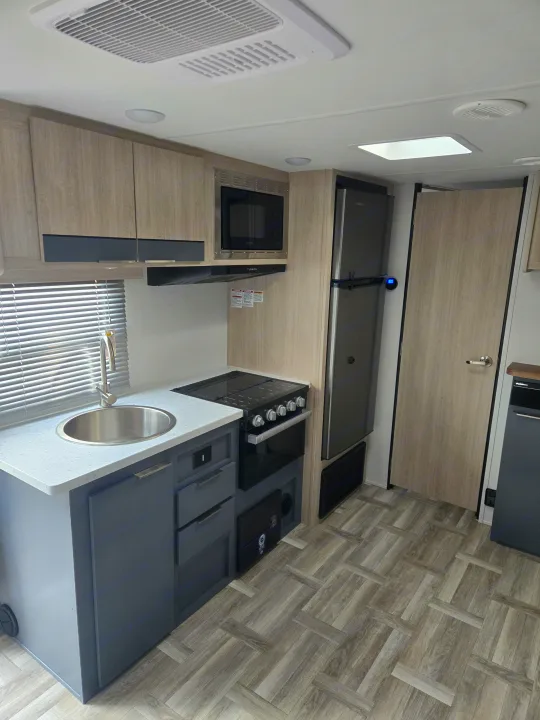 Compact & modern RV rental kitchen featuring a sink, stove, microwave, fridge, and wood-look flooring.. Prime Time Tracer LE 2024