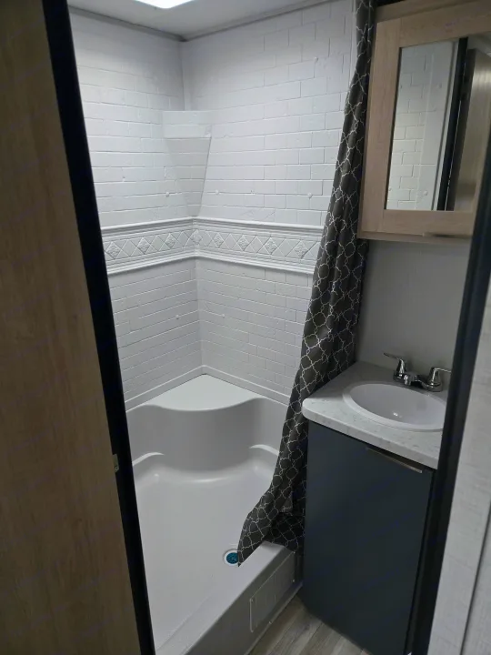 RV rental bathroom features a clean corner shower with white brick-style walls, vanity with sink, and a stylish shower curtain.. Prime Time Tracer LE 2024