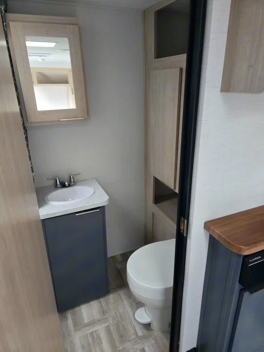 Modern compact RV rental bathroom with a gray vanity, white sink, and light wood accents. Features a toilet and mirror.. Prime Time Tracer LE 2024