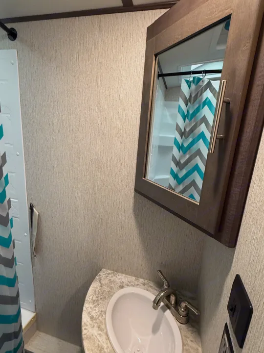 This RV rental bathroom features a sink, mirrored cabinet, and a teal chevron shower curtain.. Crossroads Sunset Trail Super Lite 2019