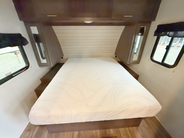 Comfortable RV rental bedroom featuring a large white mattress, dark wood storage, and side windows with outdoor views.. Crossroads Sunset Trail Super Lite 2019